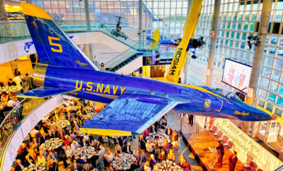 Garden City, New York, U.S. June 6, 2019. On stage are (at lectern) MICHAEL STROMER, JetBlue Chief Product Officer, Techology; and MARC MACDONNELL, Chair, Board of Directors of Cradle of Aviation, as seen from third level of atrium of CAM, during Apollo at 50 Anniversary Dinner, an Apollo astronaut tribute celebrating the Apollo 11 mission Moon landing. U.S. Navy Blue Angels Grumman F-11A Tiger jet is suspended from ceiling. Astronauts and Nassau County Executive Laura Curran, are seated at tables next to stage.