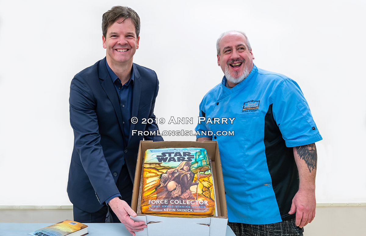 Merrick, New York, U.S. December 20, 2019. L-R, Author KEVIN SHINICK and his childhood friend BRIAN FISHMAN holds up cake Fishman decorated with cover of Shinick's book STAR WARS: FORCE COLLECTOR during book signing at North Merrick Library on Nassau County Force Collector Day. Author Shinick named home planet of Karr Nuq Sin, the main character of this canon Star Wars young adult novel, MEROKIA in honor of Merokee tribe who settled his Merrick hometown on Long Island.