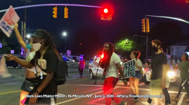 North Merrick, New York, U.S. June 4, 2020. Black Lives Matter March heads east on Jerusalem Ave and then turns north onto Bellmore Avenue, toward eastbound entrance to Southern State Parkway. Shortly before protestors arrive, Nassau County Police officers park several patrol cars at intersection to stop and divert traffic to make path for peaceful march of largely of young marchers, black and white . Many marchers wore face masks, some masks covering mouth and nose, some masks lowered below mouth as they chanted. Young black man with megaphone led the chant: megaphone man: NO JUSTICE marchers: NO PEACE megaphone man: NO RACIST marchers: POLICE Signs marchers carried included: RIP GEORGE FLOYD - IGNORANCE IS ALWAYS AFRAID OF CHANGE - BLM! - BLACK LIVES MATTER - NO RACIST POLICE