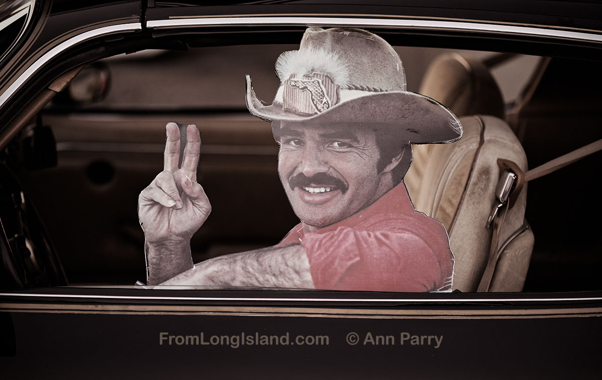 Bellmore, New York, U.S. July 30, 2021. Cardboard cutout of movie star Burt Reynolds holds up fingers making ‘V for Victory’ sign from driver’s window of 1981 Pontiac Trans Am Turbo 4.8, at the Bellmore Friday Night Car Show, held at the Bellmore Long Island Rail Road parking lot, with hundreds of visitors enjoying classic and customized cars and pleasant summer weather. (© 2021 Ann Parry, AnnParry.com)