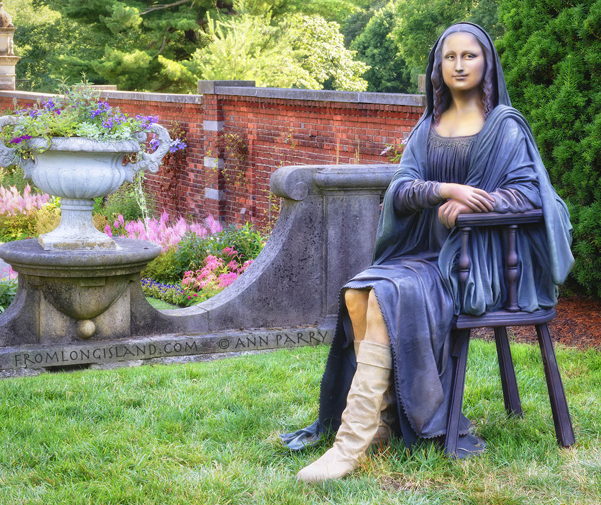 Old Westbury, New York, U.S. June 24, 2022. 'A Reason to Smile' (bronze, 2004) - a woman sitting in a chair; a wry take on the painting “Mona Lisa” by Leonardo Da Vinci - is on view at 'Re-Visiting the Familiar: Seward Johnson at the Gardens' sculpture exhibition at historic Old Westbury Gardens, on the Gold Coast of Long Island. The woman’s dark outfit is in style of early 16th century, except for off-white tall boots seen from below skirt hiked to knees. The OWG exhibit, featuring 35 individual pieces, runs from June 18 through September 5, 2022. (© 2022 Ann Parry, AnnParry.com)