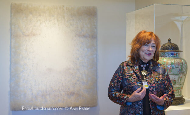 Roslyn Harbor, New York, USA. January 2, 2015. Docent LINDA SCHWARTZ shares information about the artwork exhibits at the Nassau County Museum of Art China Now and Then Exhibit on Long Island. Artwork on wall by Chinese artist Lin Tianmiao is Digital Photograph on canvas with thread, with eyes nose and lips of face faintly visible. (© Ann Parry, annParry.com)