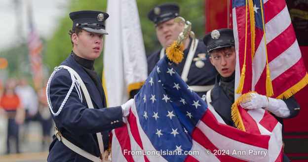 Merrick, New York, U.S. May 27, 2024. Young men wearing firefighter ceremonial uniforms, including Merrick Hook and Ladder, are wrapping up large American Flags they carried while marching in Merrick Memorial Day Parade on Long Island. (© Ann Parry, annparry.com)